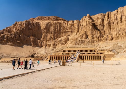 Luxor, Egypt - 2 November 2024: Tourists walk to the Mortuary Temple of Hatshepsut which stands majestically against the dramatic cliffs