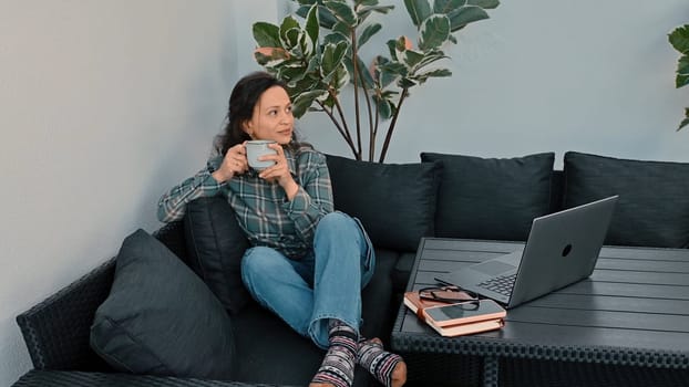 A serene image of a woman enjoying coffee in a cozy setup, illustrating remote work lifestyle. A laptop and personal items nearby emphasize modern work flexibility and leisure.