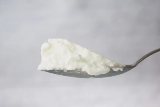 A spoon holds a generous scoop of creamy yogurt with a smooth texture.