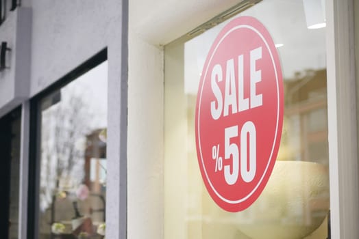 Bright red sale sign indicates fifty percent off in a retail window.