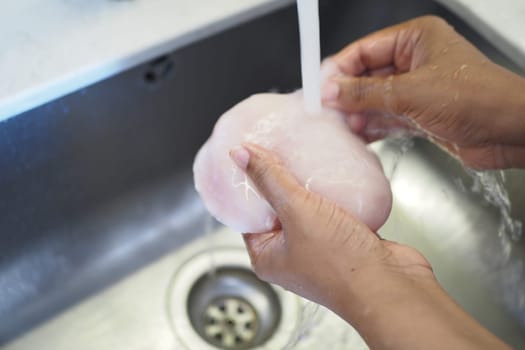 Water flows over raw chicken being cleaned in the sink.