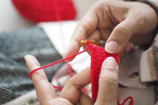 Hands skillfully working on a red crochet project while relaxing indoors.