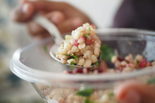 A hand holds a spoonful of pearl barley salad with vibrant vegetables.