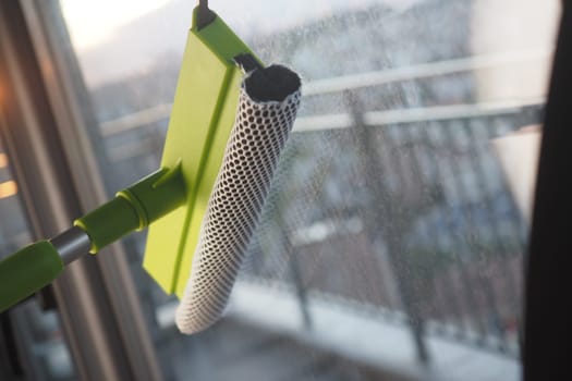 A bright green cleaning tool is removing dirt from a window.