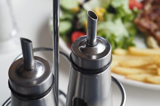 Silver condiment containers are placed beside a salad and fries.
