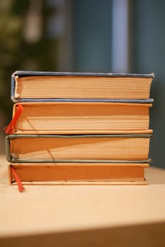 Four vintage books are neatly stacked on a wooden table's surface.