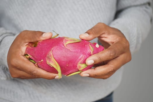 A person showcases a vibrant dragon fruit in their hands indoors.