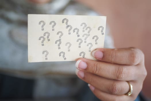 A person considers a card covered in question marks while pondering.