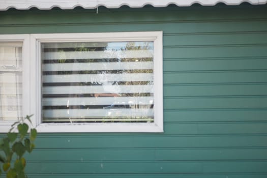 A quiet neighborhood house features a green exterior and striped curtains.