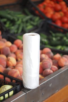A roll of cleaning paper sits by fresh peaches and veggies at market.
