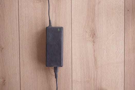 Black power adapter positioned on a light wood background.