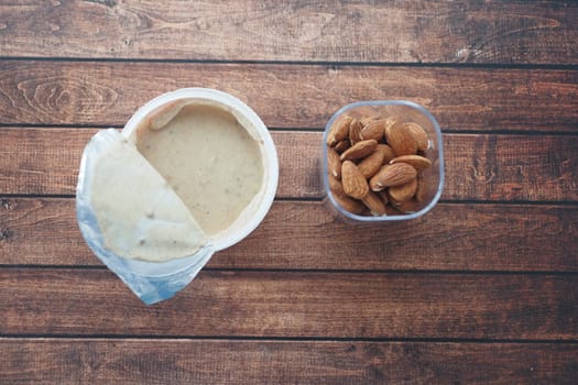 A container of almond butter and a bowl of almonds shown on a table.