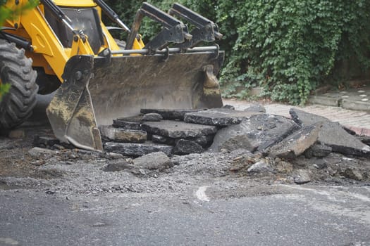 Construction crew uses a loader to lift broken asphalt for repairs.