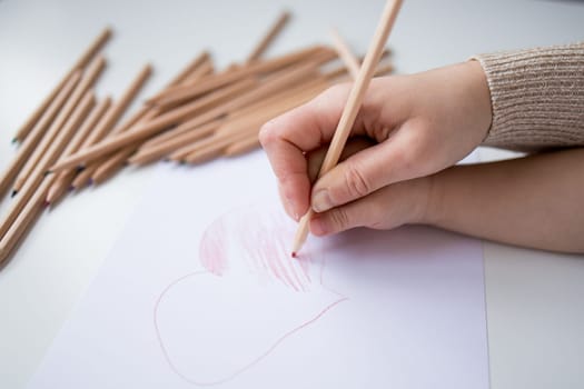 Female hand drawing heart with colored pencils on white paper.