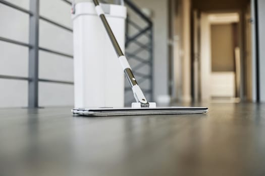 Cleaning supplies: mop and bucket with wringer sitting on wooden laminate floor in modern corridor, wet equipment tools, housekeeping concept. Emphasizing home sanitation, cleanliness, hygiene
