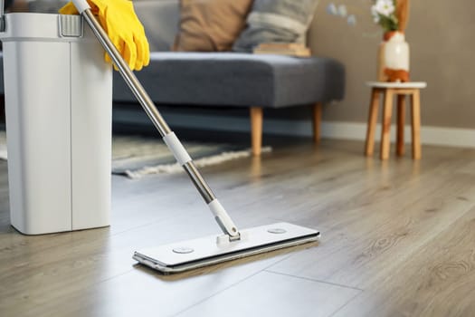 Cleaning supplies: mop, gloves, bucket with wringer sitting on wooden laminate floor in modern living room, wet equipment tools, housekeeping concept. Emphasizing home sanitation, cleanliness, hygiene