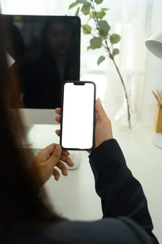 Over shoulder view of woman holding smartphone with blank screen, sitting at a modern workspace.