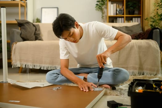Man assembling a piece of furniture using an electric screwdriver in a living room.