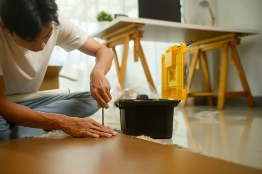 Man using a screwdriver assembling new piece of furniture in bright home.