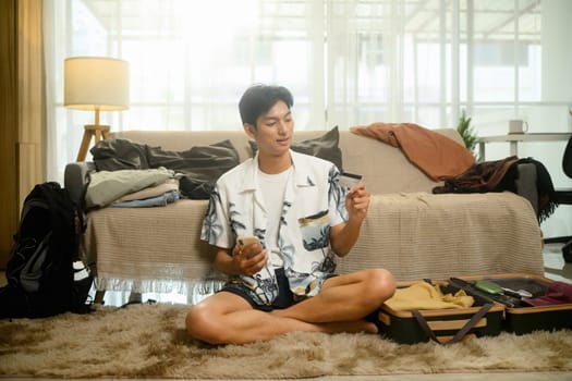 Man holding credit card booking flights and accommodations on mobile phone for summer trip.