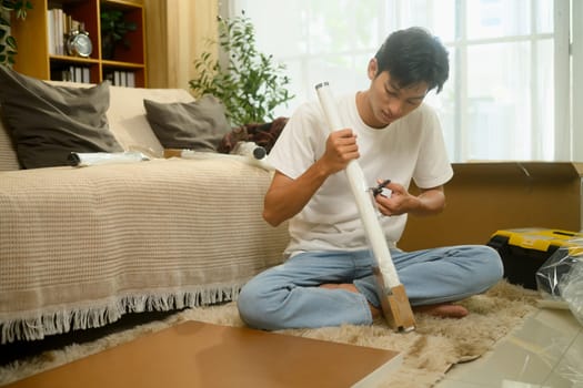 Young asian man unpacking a table leg preparing to assemble a new piece of furniture in his living room.