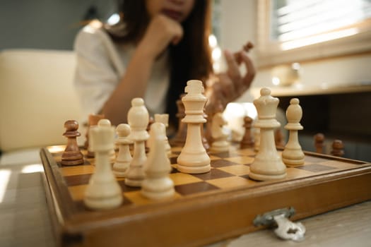Wooden chessboard with pieces in play with person in the background considers their next move.