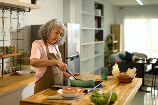Senior woman wearing apron preparing breakfast in a stylish kitchen.