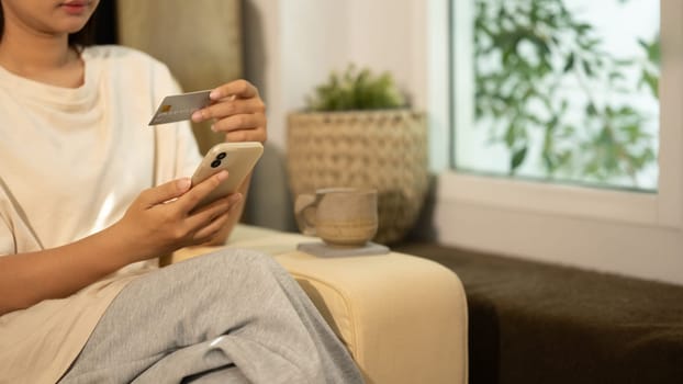 Woman holding credit card while using smartphone for online transactions or digital payments.