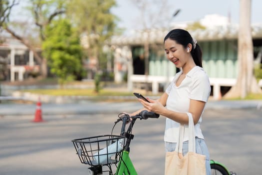 A young woman smiles while using her phone next to her green bicycle, representing modern and sustainable commuting.