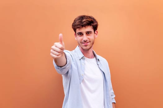 young man giving a thumb up gesture while smiling looking at camera in a positive and friendly mood suggesting that he is happy and content, copyspace for text