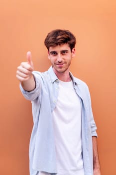 young man giving a thumb up gesture while smiling looking at camera in a positive and friendly mood suggesting that he is happy and content, copyspace for text