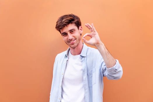 young man doing ok sign with hand while smiling looking at camera in a positive and friendly mood suggesting that he is happy and content, copyspace for text