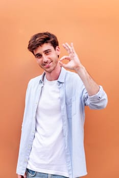 young man doing ok sign with hand while smiling looking at camera in a positive and friendly mood suggesting that he is happy and content, copyspace for text