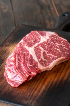 Thick, marbled ribeye steak resting on a rustic board, seasoned with salt and pepper