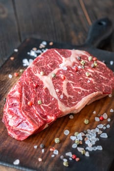 Thick, marbled ribeye steak resting on a rustic board, seasoned with salt and pepper