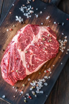 Thick, marbled ribeye steak resting on a rustic board, seasoned with salt and pepper