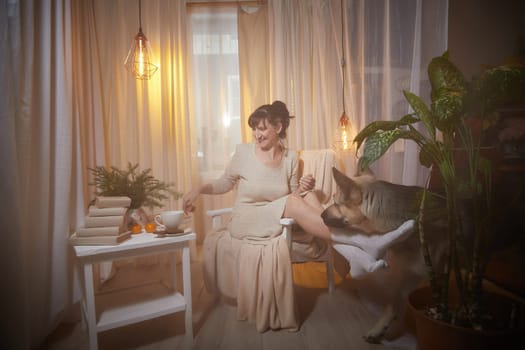 A middle-aged woman sits comfortably in her cozy apartment, savoring the evening atmosphere with a sense of relaxation and pleasure.