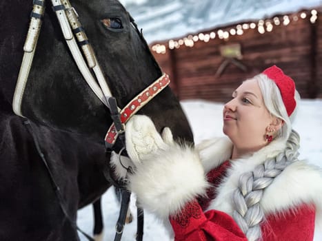 A girl in a national dress interacts with a horse in a winter setting, celebrating the Maslenitsa festival.