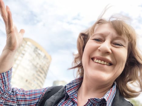 A middle-aged woman captures a joyful moment with a selfie during her summer trip in a lively city atmosphere.