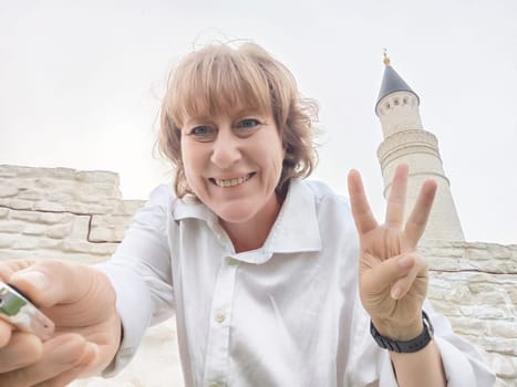 A cheerful woman takes a selfie while visiting a historic site, showcasing her excitement as a traveler enjoying her excursion.