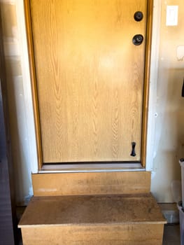 Broomfield, Colorado, USA-February 23, 2025-A wooden interior door leading from the garage into the home, featuring a small step for entry. The door has a natural wood finish with a black handle and deadbolt. Surrounding the door is a beige-painted wall with visible signs of wear.