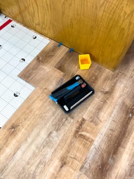 Broomfield, Colorado, USA-February 23, 2025-A close-up of flooring installation tools placed on a newly installed wood-look floor. A tapping block, pull bar, and spacers are visible alongside underlayment, indicating an ongoing home improvement project. The tools are positioned near kitchen cabinetry, highlighting the renovation process.
