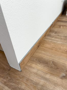 Broomfield, Colorado, USA-February 16, 2025-Close-up of a newly installed wood baseboard matching the wood-look flooring in a home renovation project. The baseboard is partially installed, with a visible gap between two sections. The flooring has a warm wood grain finish, complementing the clean white wall.
