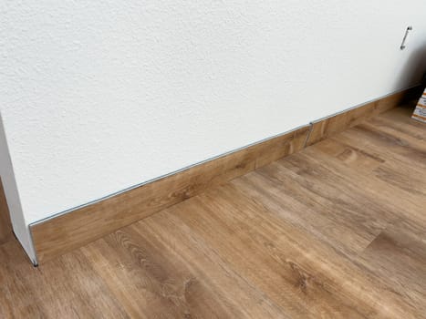 Broomfield, Colorado, USA-February 16, 2025-Close-up of a newly installed wood baseboard matching the wood-look flooring in a home renovation project. The baseboard is partially installed, with a visible gap between two sections. The flooring has a warm wood grain finish, complementing the clean white wall.