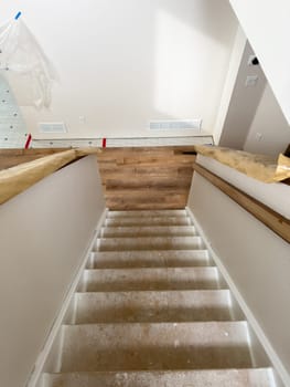 Broomfield, Colorado, USA-February 15, 2025-A staircase under renovation in a home improvement project. The steps remain unfinished, while the upper floor showcases newly installed wood-look flooring. Protective paper is wrapped around the handrails, and construction materials are visible in the background.