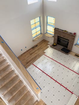 Broomfield, Colorado, USA-January 26, 2025-A spacious living room undergoing flooring installation, with wood-look planks partially laid over an underlayment. The fireplace and large windows bring warmth and natural light to the space. The staircase and walls are prepped for renovation, indicating an ongoing home improvement project.