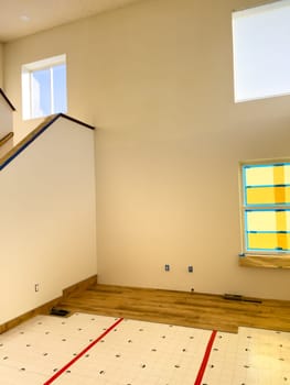 Broomfield, Colorado, USA-January 26, 2025-A home interior undergoing renovation with partially installed wood-look flooring. The underlayment is still visible, showing progress in the flooring installation process. The high ceilings, large windows, and staircase add to the spacious and modern feel of the space.