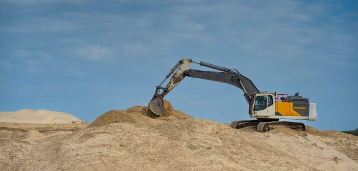 Heavy machinery is actively moving sand along the coastline under a clear blue sky, focusing on erosion control efforts during daylight hours in a coastal area.