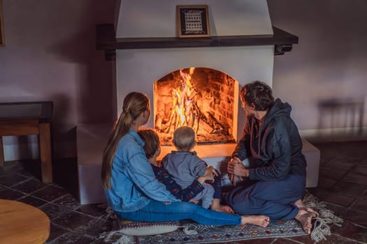 Family bonding by the fireplace during cozy winter evening. Warm and peaceful family moment indoors. Togetherness, love, and relaxation concept. A warm and inviting scene featuring a lit fireplace with glowing firewood and candles. A colorful traditional rug and pillow lie on the floor, creating a cozy atmosphere. Home, relaxation, and rustic comfort concept.