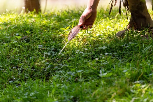 Man in Indian clothing picks up a bird's feather in a meadow on the banks of a stream